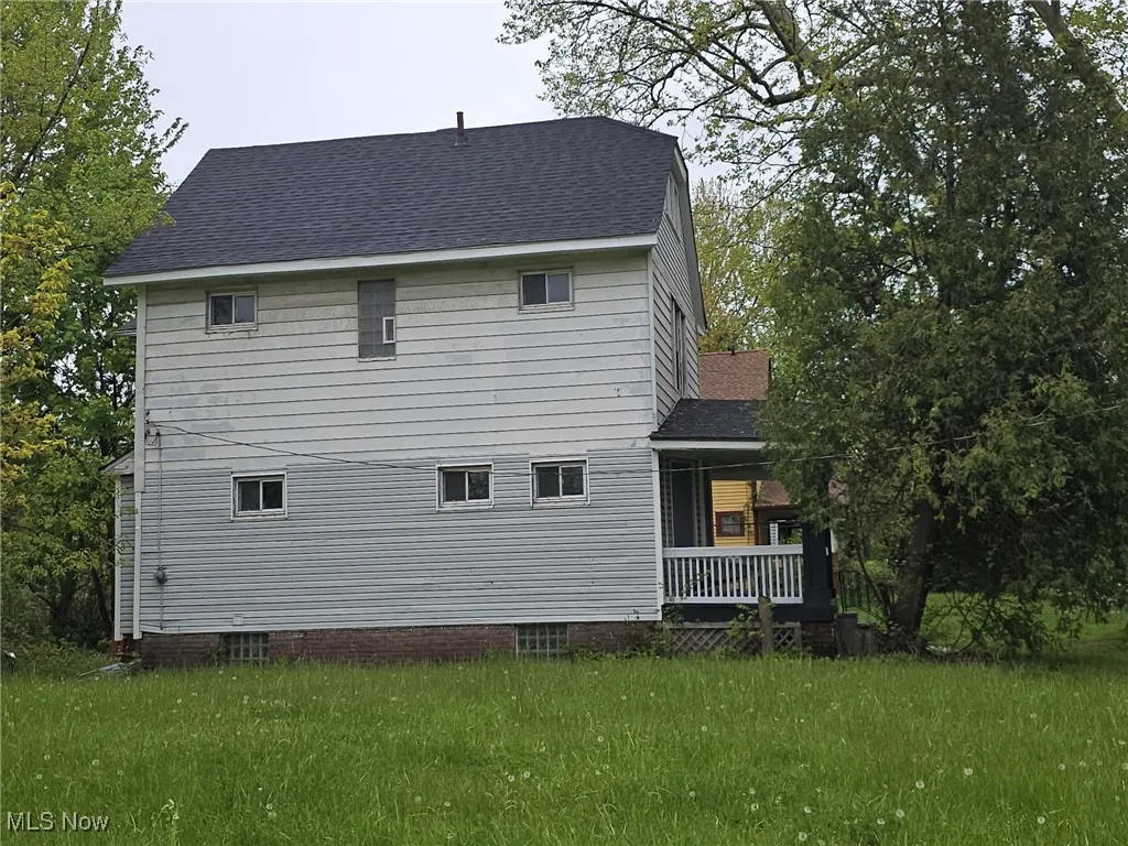 View of side of property with roof with shingles, a porch, and a lawn