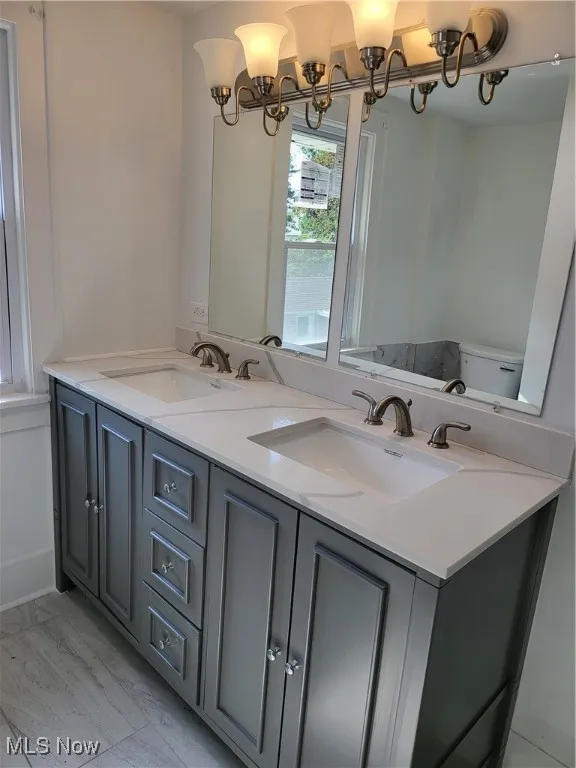 Bathroom with double vanity, marble look tiles, and a chandelier