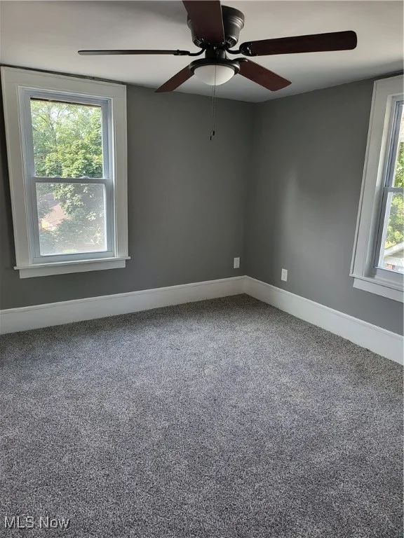 Carpeted spare room featuring baseboards and ceiling fan