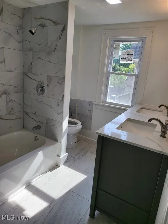 Bathroom featuring a wainscoted wall, vanity, shower / bathtub combination, and marble look tile flooring