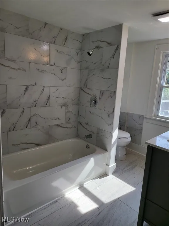Bathroom featuring marble finish flooring, wainscoting, bathing tub / shower combination, and vanity