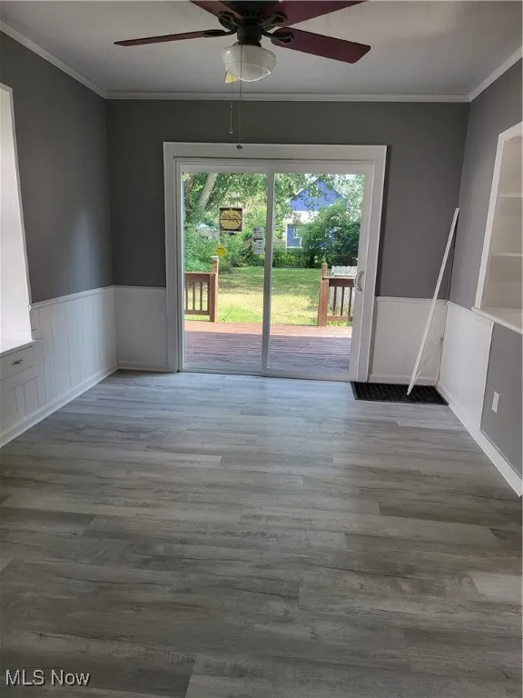 Spare room featuring ornamental molding, a wainscoted wall, a ceiling fan, and wood finished floors