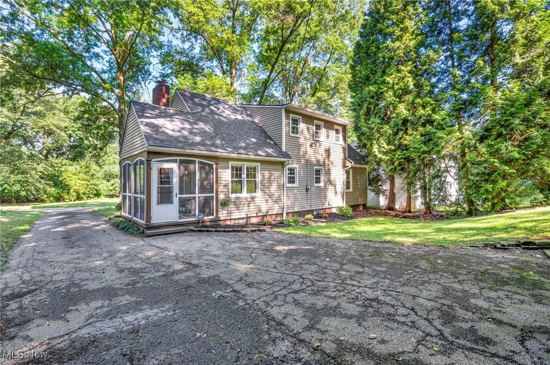 View of side of home with attached screened-in porch, view of partially wooded backyard, newly shingled roof and asphalt driveway.