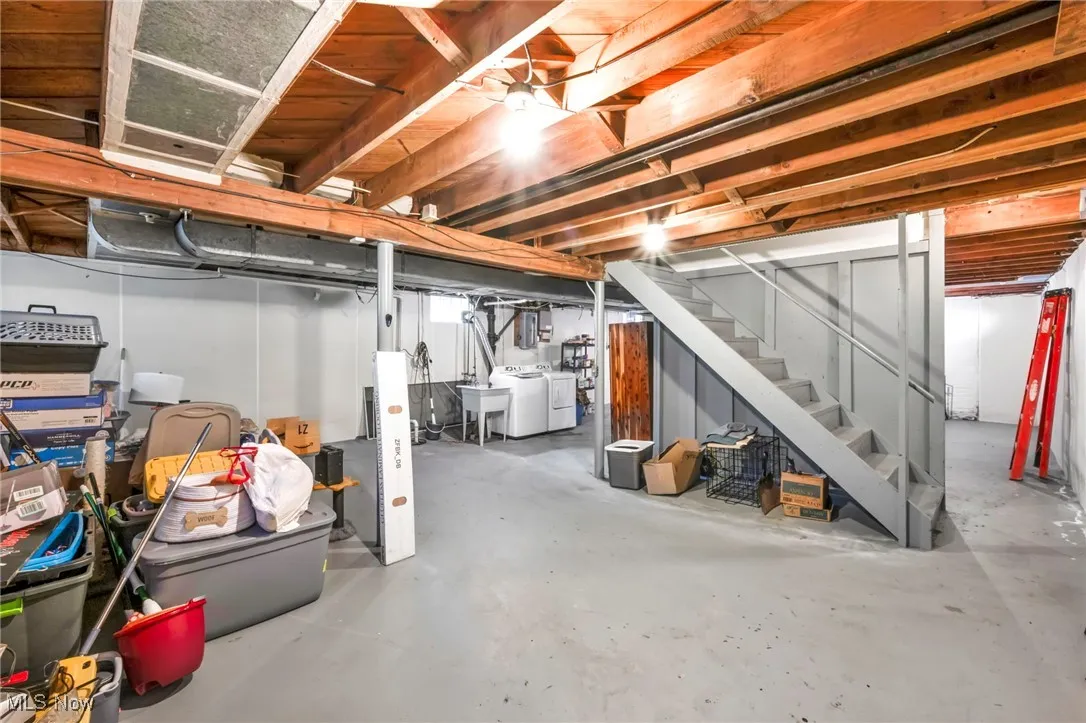 Unfinished basement to the right of the stairs showing ample storage space and included washer and dryer.
