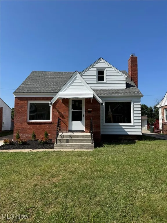 Bungalow-style home with roof with shingles, entry steps, a chimney, and a front lawn