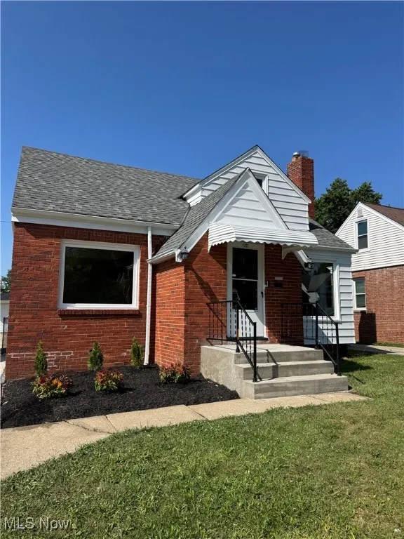 View of front of house featuring roof with shingles, a chimney, a front lawn, and brick siding