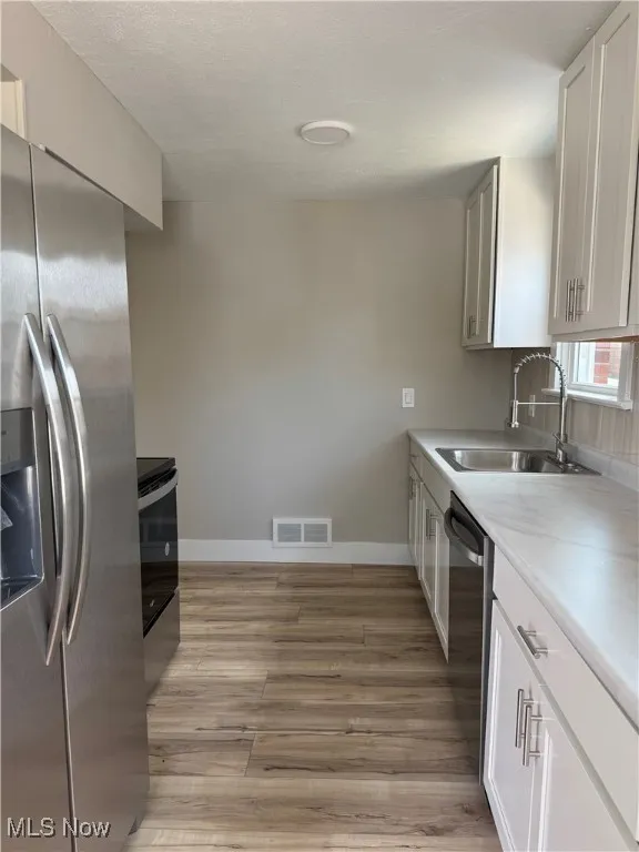 Kitchen featuring stainless steel appliances, light wood-type flooring, light countertops, and white cabinetry