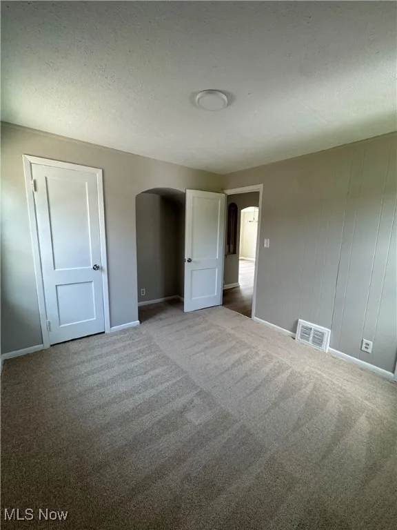 Unfurnished bedroom with a textured ceiling, arched walkways, and carpet floors