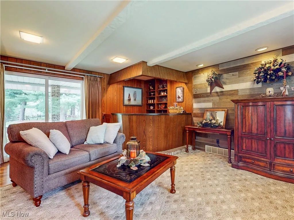 Carpeted living room featuring wood walls, beamed ceiling, built in shelves, and recessed lighting
