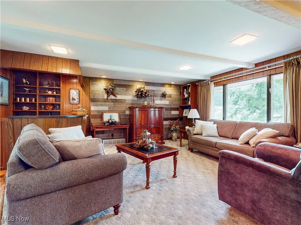 Carpeted living area with wooden walls, built in features, and beam ceiling