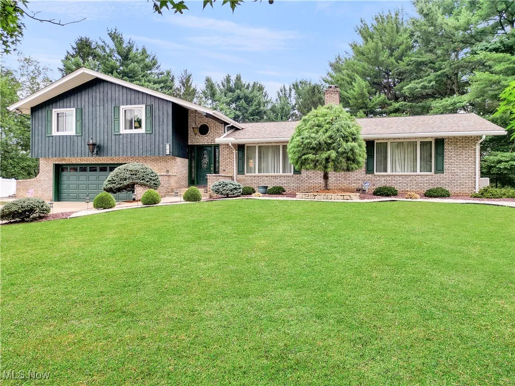 Split level home with a chimney, a garage, a front lawn, and brick siding
