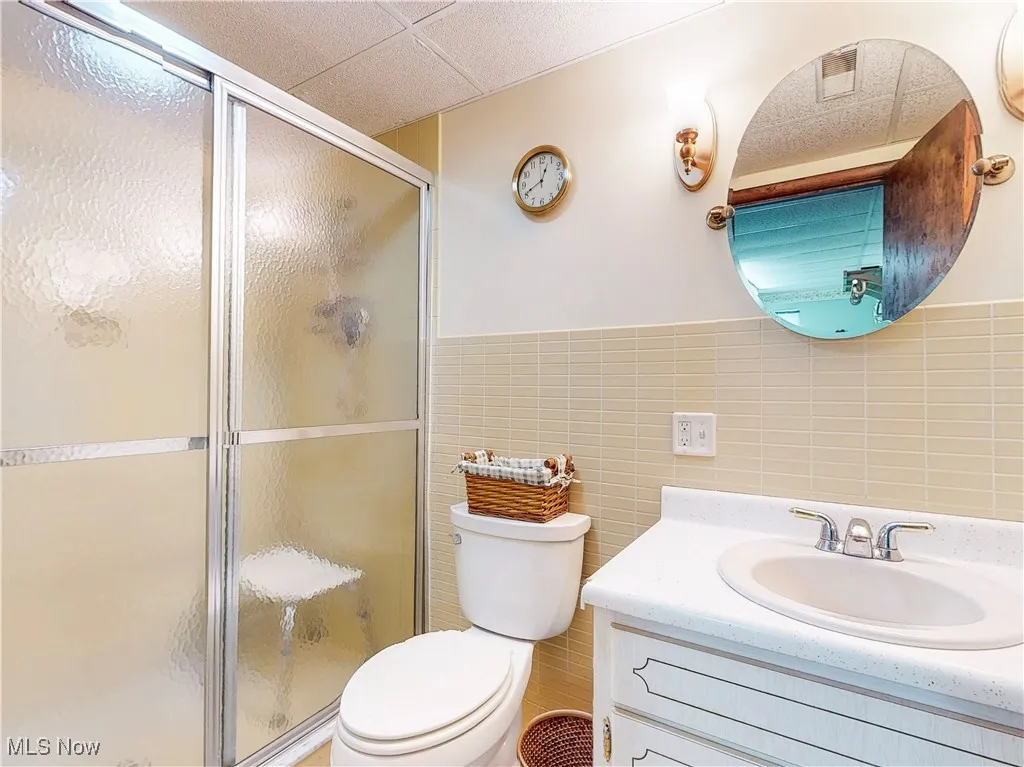Bathroom with tile walls, a wainscoted wall, a shower stall, vanity, and a drop ceiling
