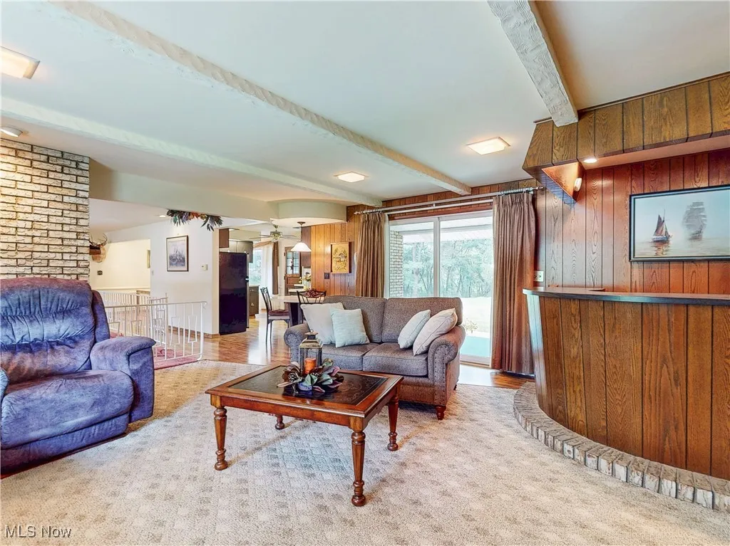 Living area featuring wooden walls, beam ceiling, light colored carpet, and arched walkways