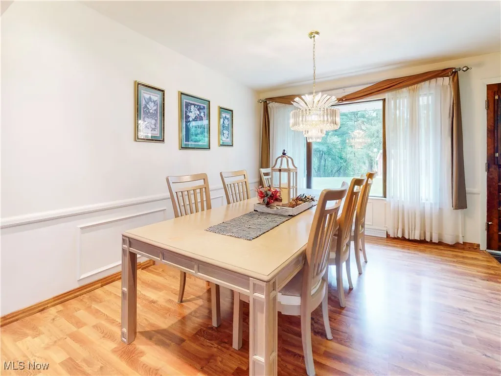 Dining area with a decorative wall, light wood-type flooring, a wainscoted wall, and a chandelier