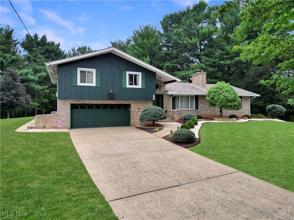 Tri-level home featuring an attached garage, a front yard, brick siding, and concrete driveway