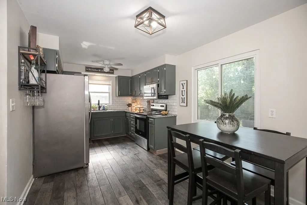 Kitchen featuring appliances with stainless steel finishes, dark wood-style flooring, backsplash, gray cabinets, and a ceiling fan