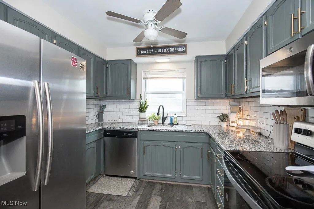 Kitchen featuring stainless steel appliances, dark wood-style floors, light stone counters, decorative backsplash, and a ceiling fan
