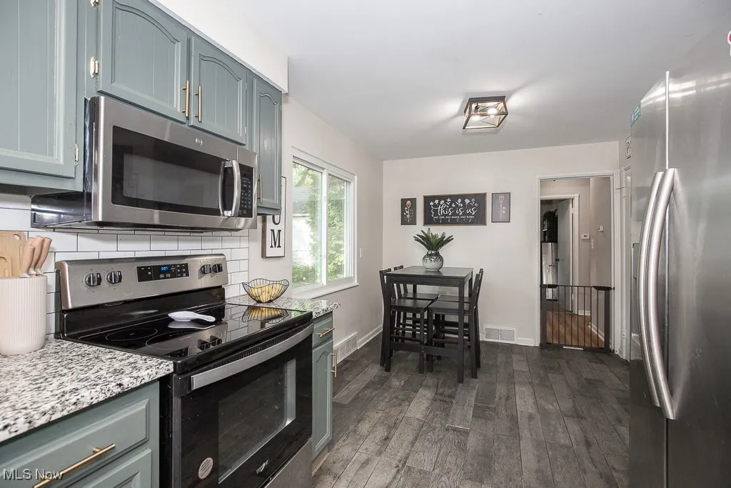 Kitchen featuring appliances with stainless steel finishes, dark wood finished floors, decorative backsplash, light stone counters, and gray cabinets