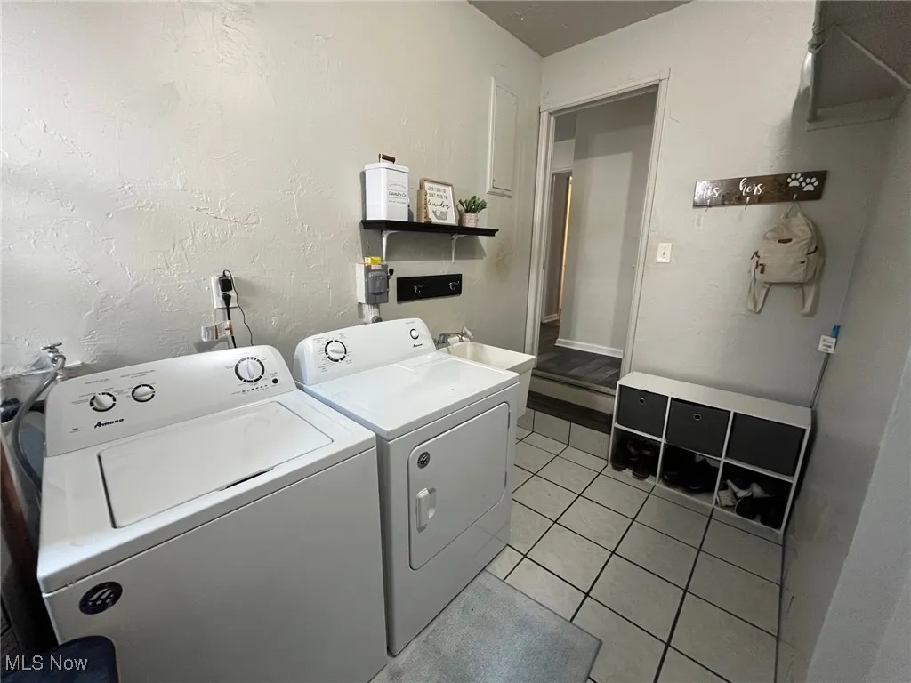 Washroom with washing machine and dryer, light tile patterned flooring, and a textured wall