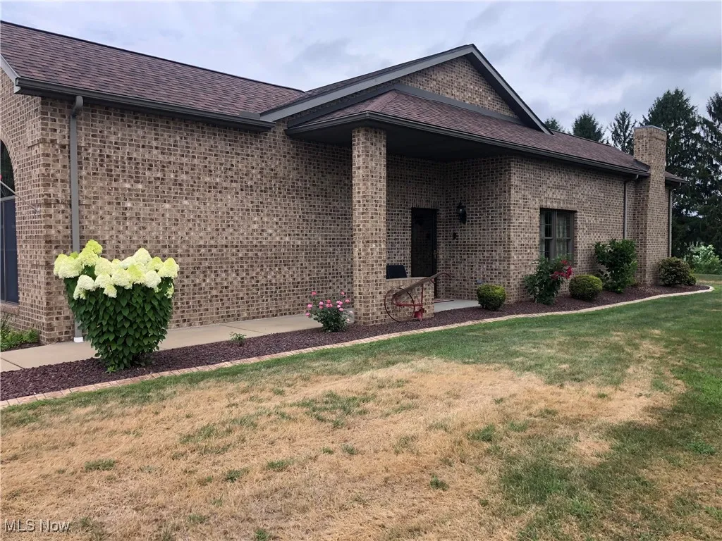 View of front facade featuring a chimney, a front lawn, brick siding, and roof with shingles