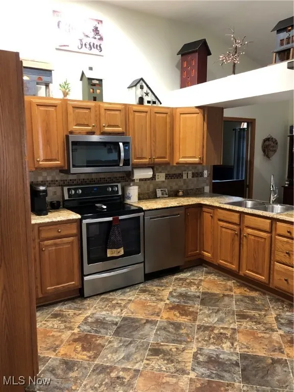 Kitchen featuring stove, dishwasher, stone finish flooring, brown cabinets, and a towering ceiling