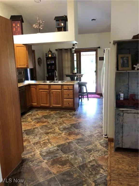 Kitchen with a peninsula, stone finish flooring, refrigerator, light countertops, and brown cabinets