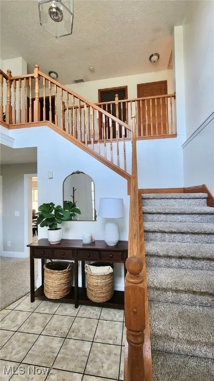 Stairway with tile patterned flooring, a textured ceiling, carpet flooring, and a high ceiling