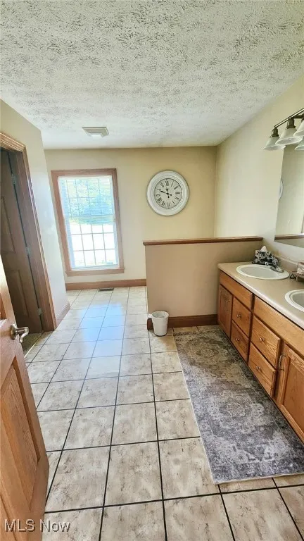 Bathroom featuring double vanity, a textured ceiling, and tile patterned floors