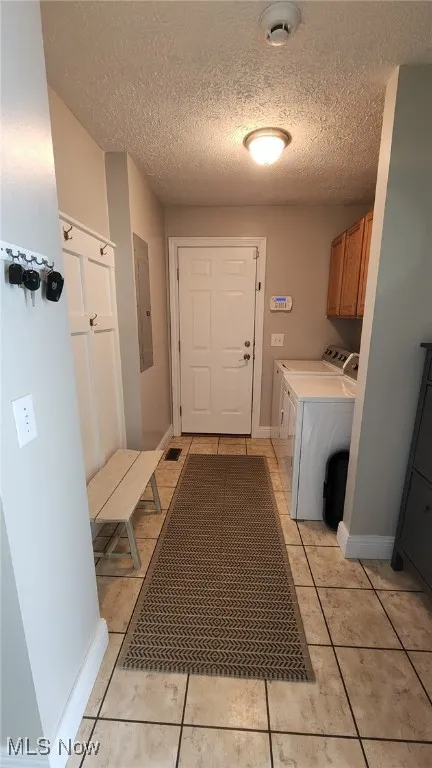 Washroom featuring washer and dryer, cabinet space, a textured ceiling, and light tile patterned floors