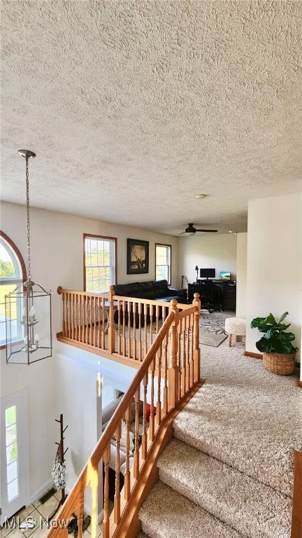 Stairs with healthy amount of natural light, a textured ceiling, tile patterned flooring, a chandelier, and a ceiling fan