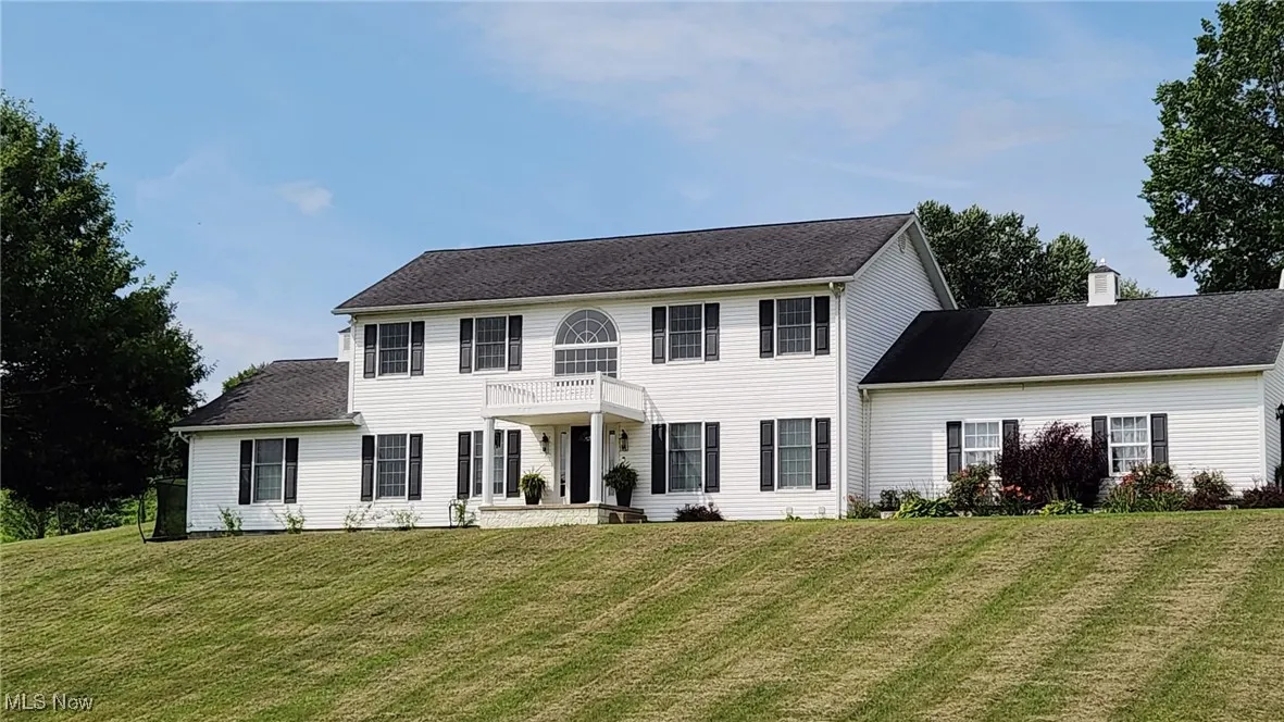 Colonial house with a front yard, a chimney, a balcony, and a shingled roof