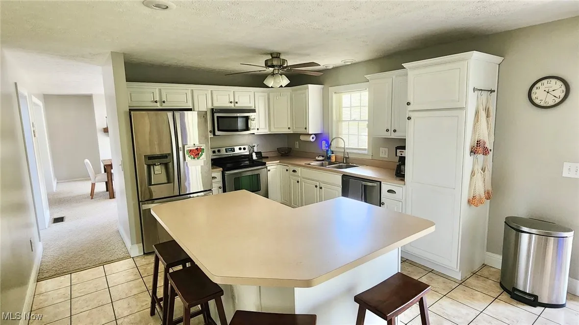 Kitchen with stainless steel appliances, light tile patterned floors, a kitchen breakfast bar, a textured ceiling, and white cabinets