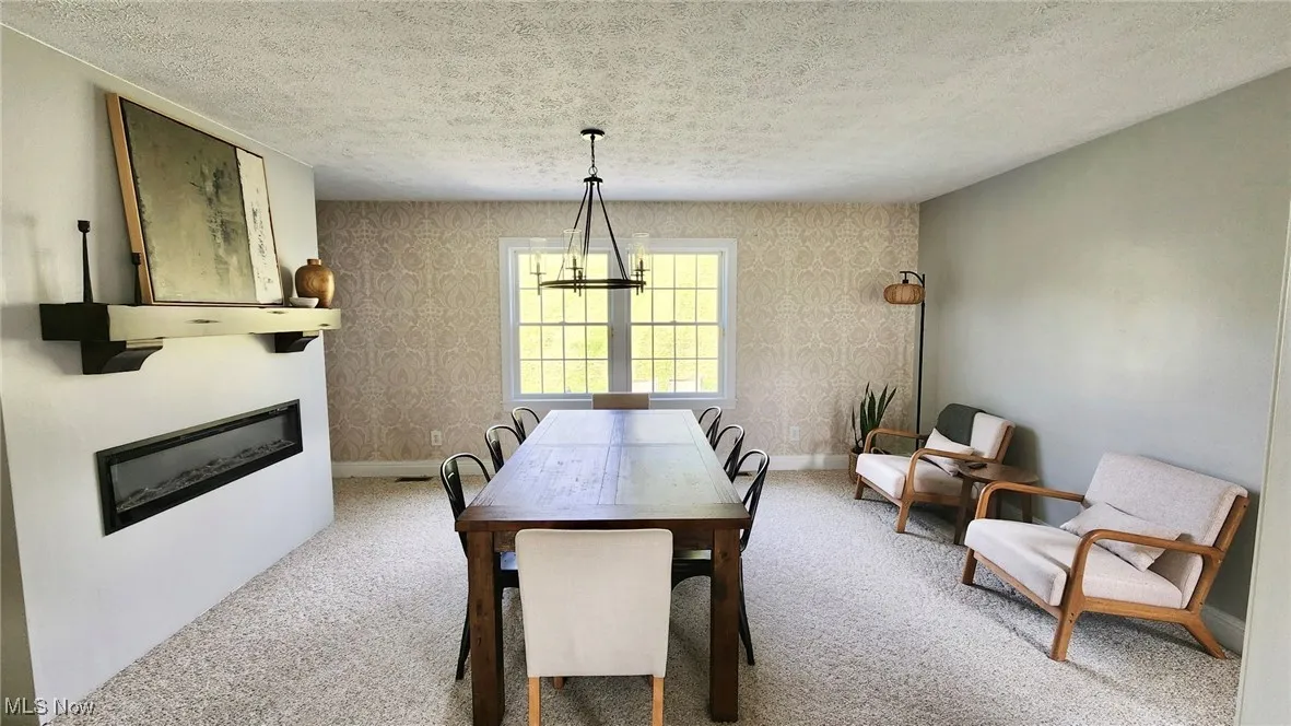 Dining area featuring a textured ceiling, a glass covered fireplace, light colored carpet, wallpapered walls, and a chandelier