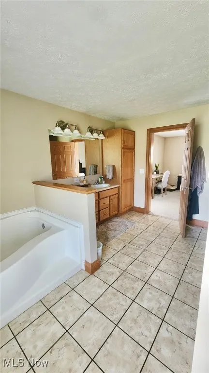Bathroom with vanity, a textured ceiling, a bath, and tile patterned flooring