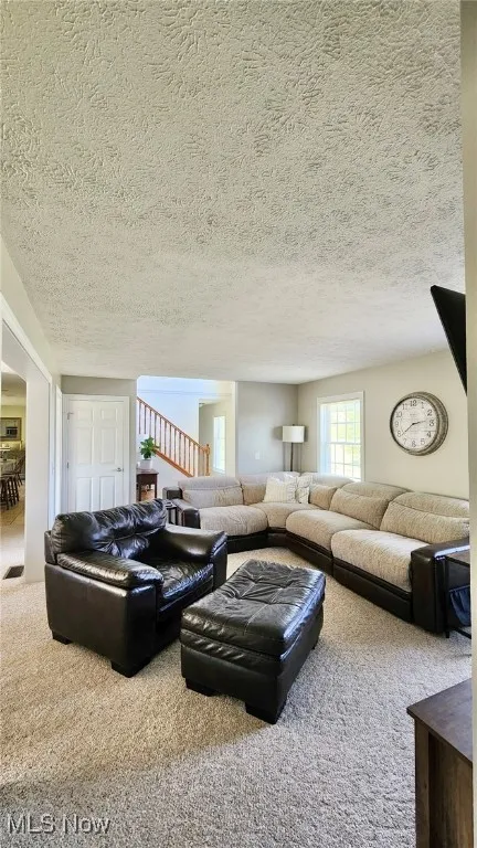 Living room with carpet floors, a textured ceiling, and stairway