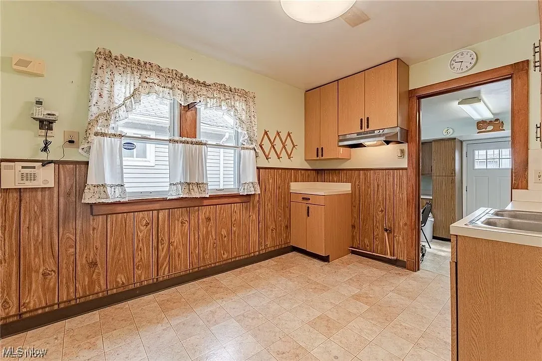 Kitchen featuring a wainscoted wall, wooden walls, light flooring, under cabinet range hood, and light countertops