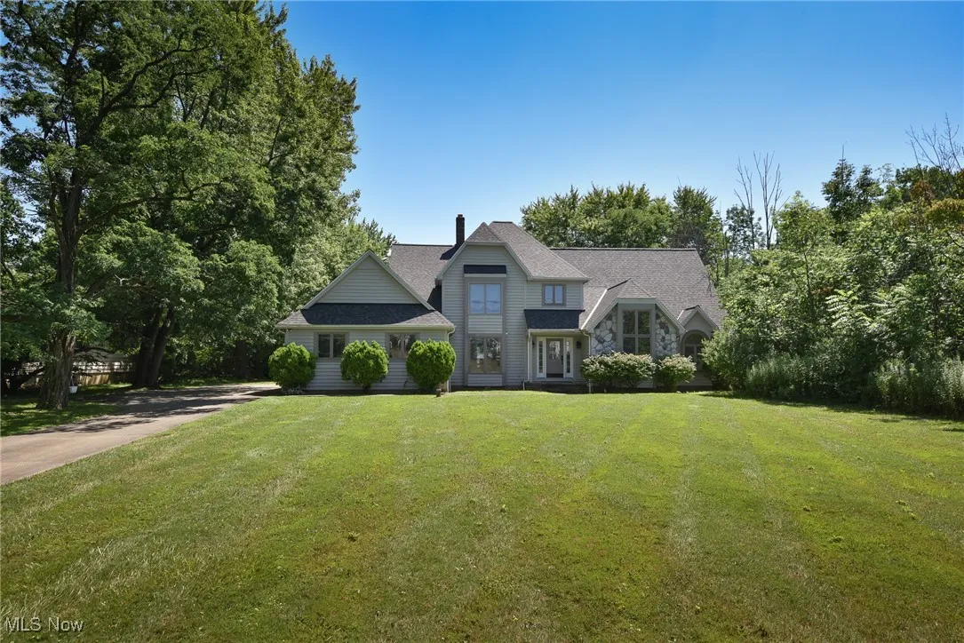 Shingle-style home with a front yard, a chimney, stone siding, and view of scattered trees