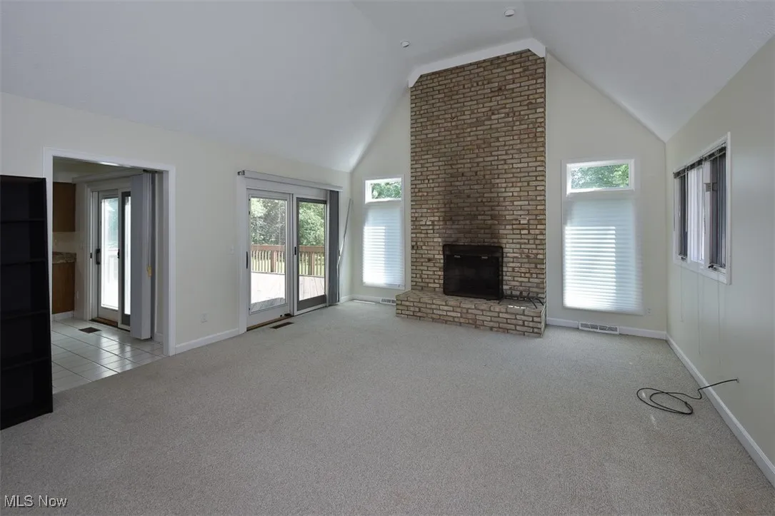 Unfurnished living room featuring carpet floors, a brick fireplace, and high vaulted ceiling