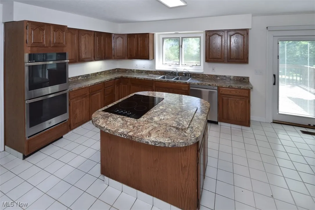Kitchen featuring light tile patterned floors, stainless steel appliances, a center island, and dark countertops