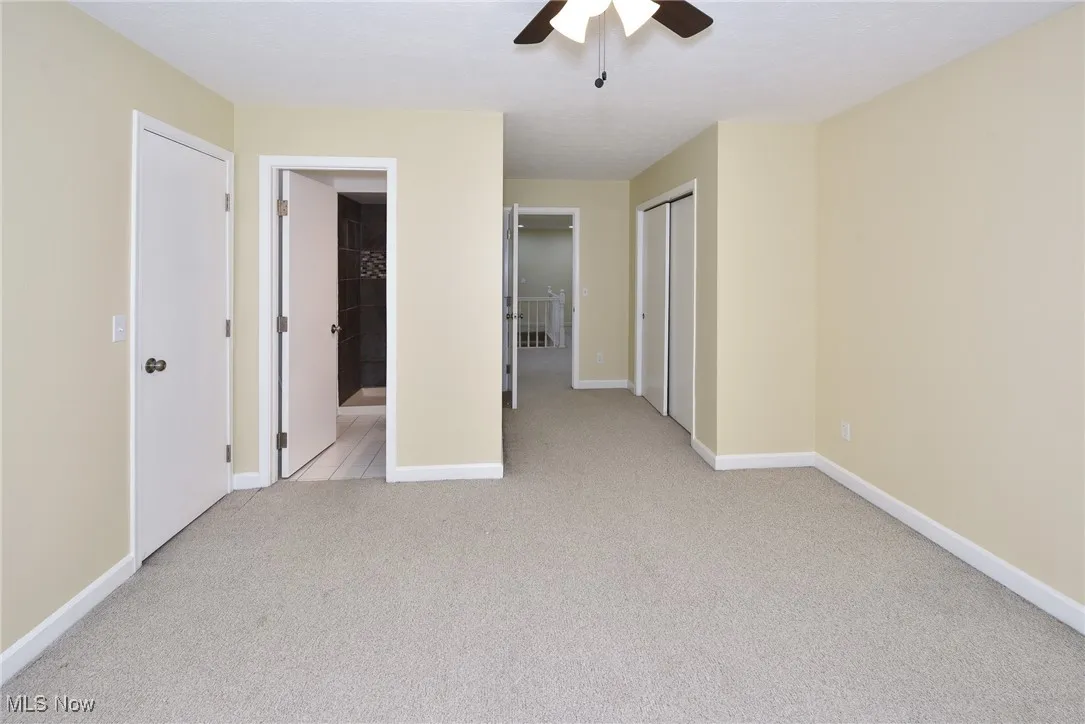 Unfurnished bedroom featuring light colored carpet, ensuite bath, and ceiling fan