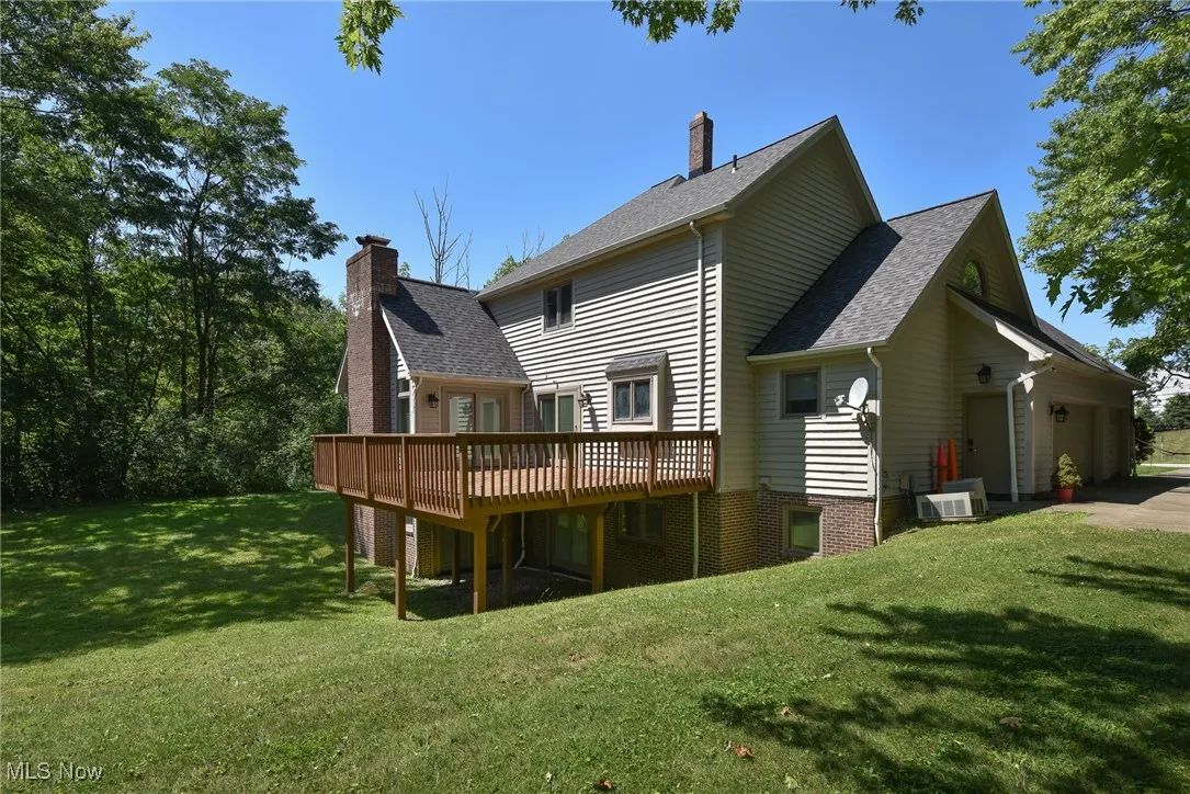 Rear view of house with a deck, roof with shingles, a lawn, and a chimney