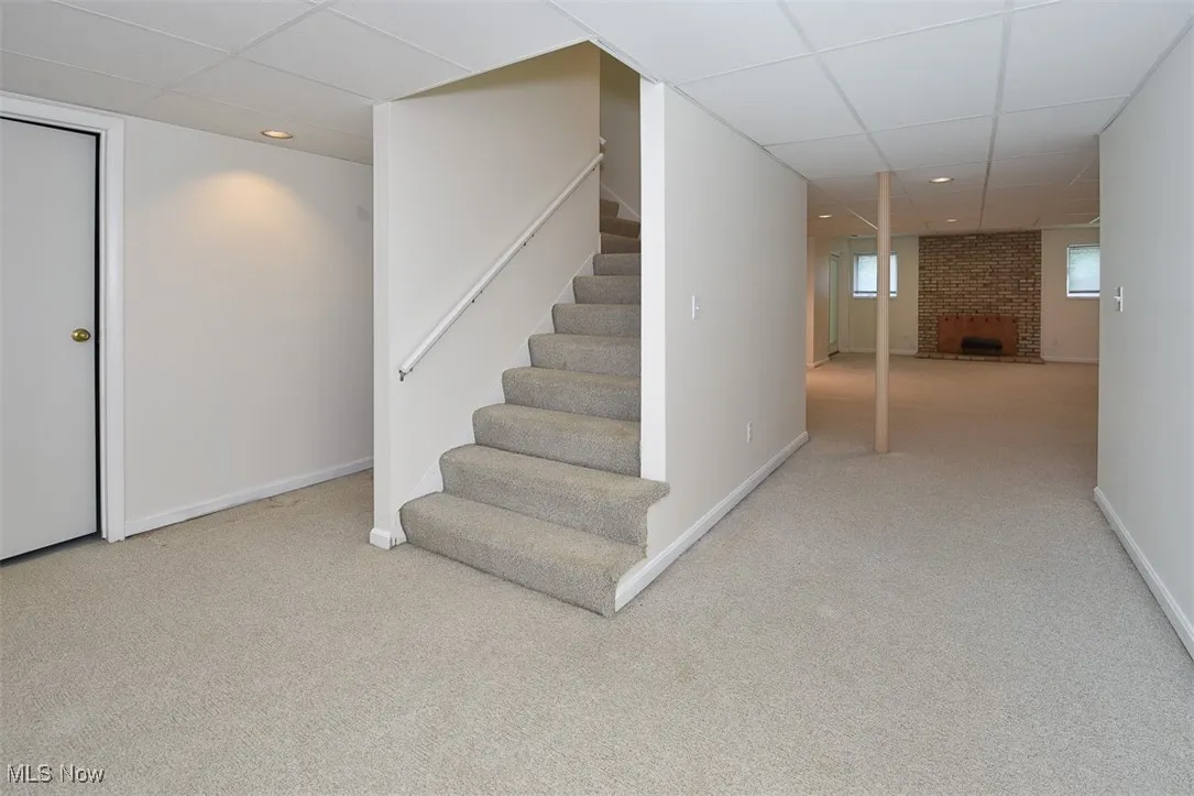 Basement featuring a paneled ceiling, carpet flooring, a brick fireplace, recessed lighting, and stairway