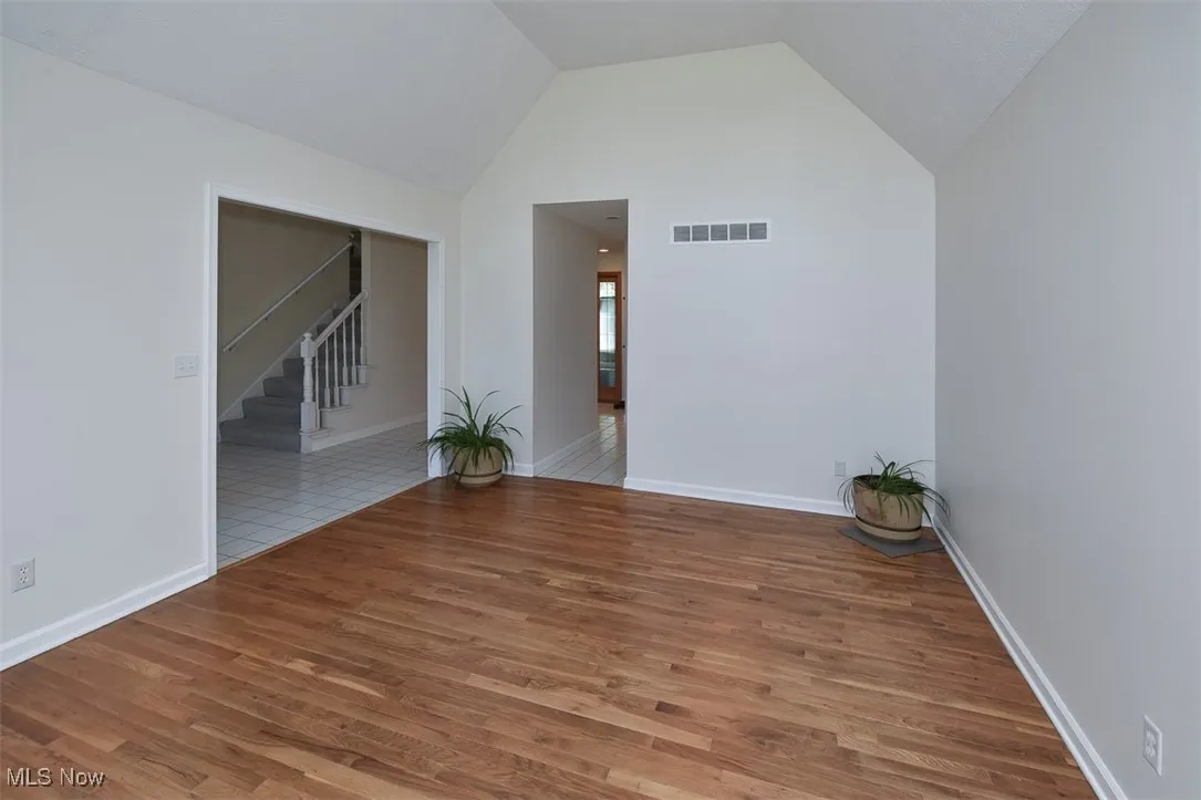 Unfurnished room with stairs, wood finished floors, and high vaulted ceiling