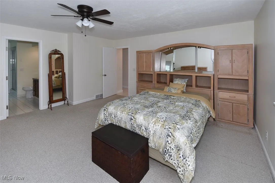 Bedroom with light colored carpet, a ceiling fan, and connected bathroom