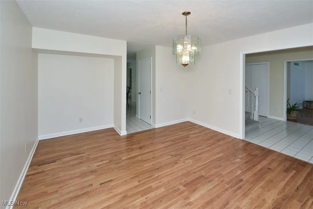 Unfurnished dining area featuring a chandelier, light wood-type flooring, stairs, and a textured ceiling