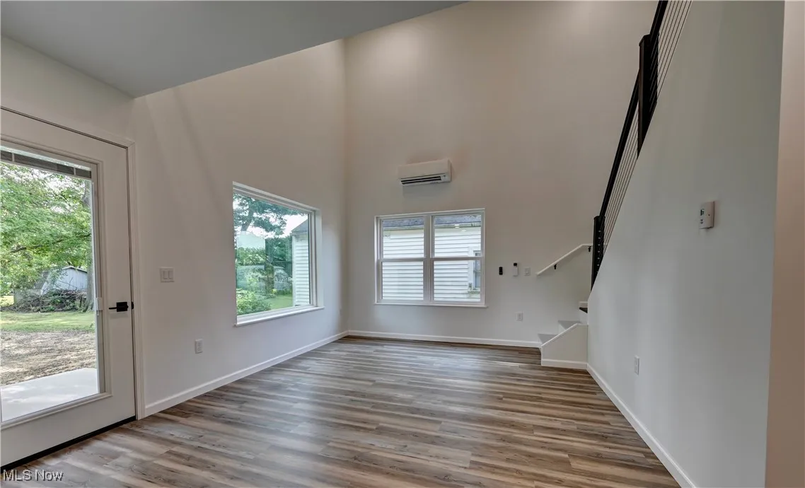 Unfurnished living room with plenty of natural light, stairway, wood finished floors, a high ceiling, and a wall mounted air conditioner