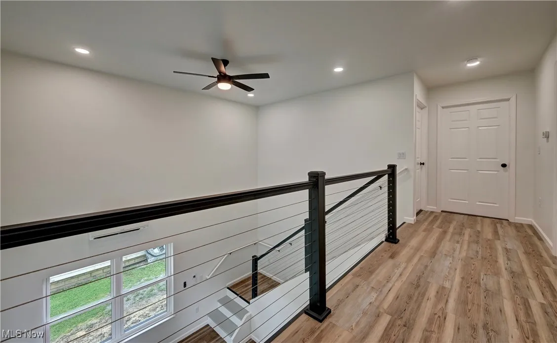 Corridor with an upstairs landing, light wood-style flooring, and recessed lighting