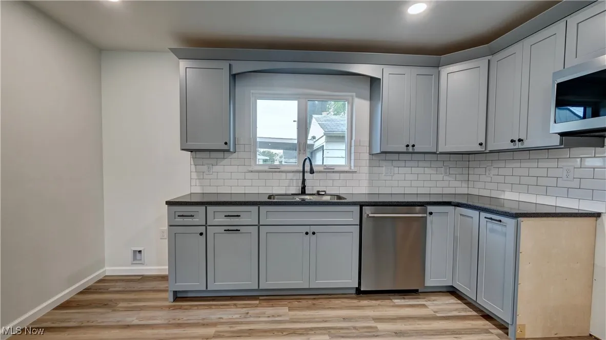 Kitchen featuring dark countertops, stainless steel appliances, tasteful backsplash, light wood-style flooring, and recessed lighting