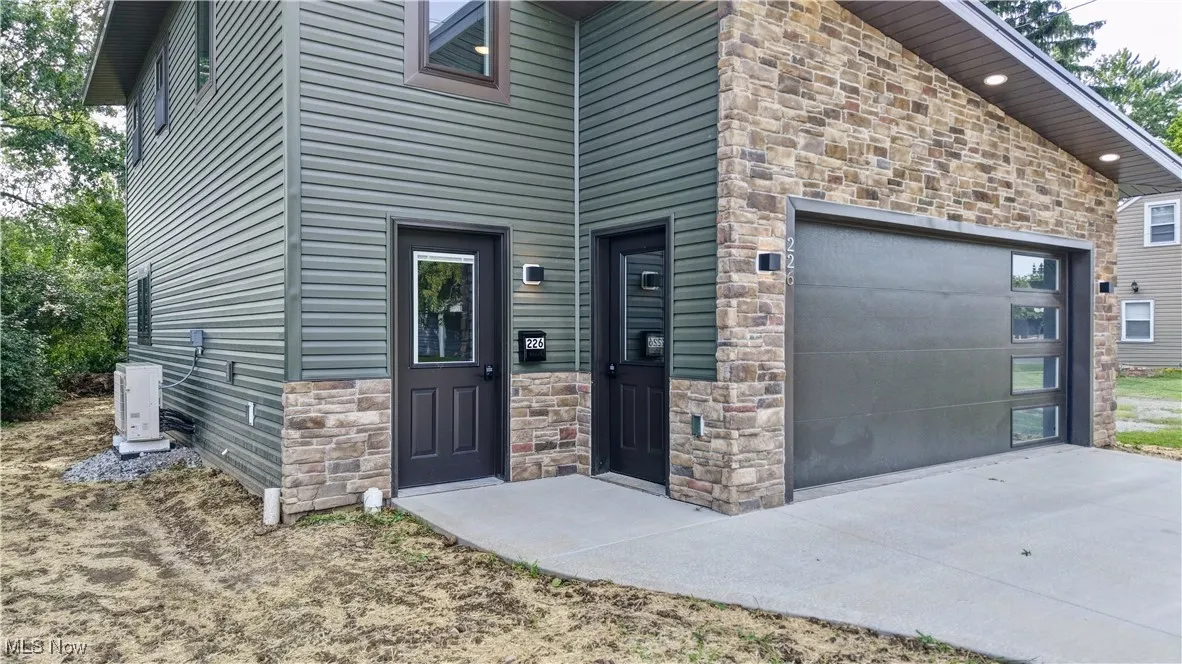 View of exterior entry featuring stone siding, an attached garage, and driveway