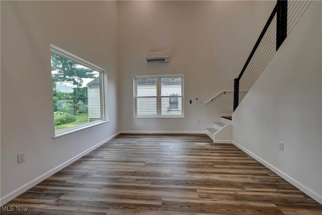 Unfurnished living room with stairway, wood finished floors, a towering ceiling, and an AC wall unit